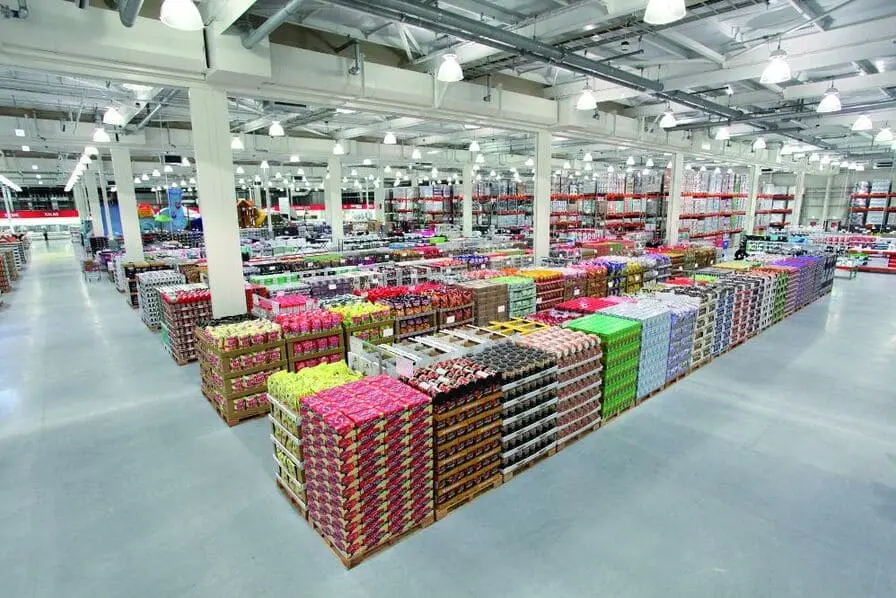 Vue panoramique de l'intérieur d'un entrepôt Costco montrant des allées spacieuses et des produits stockés en gros sur des palettes.