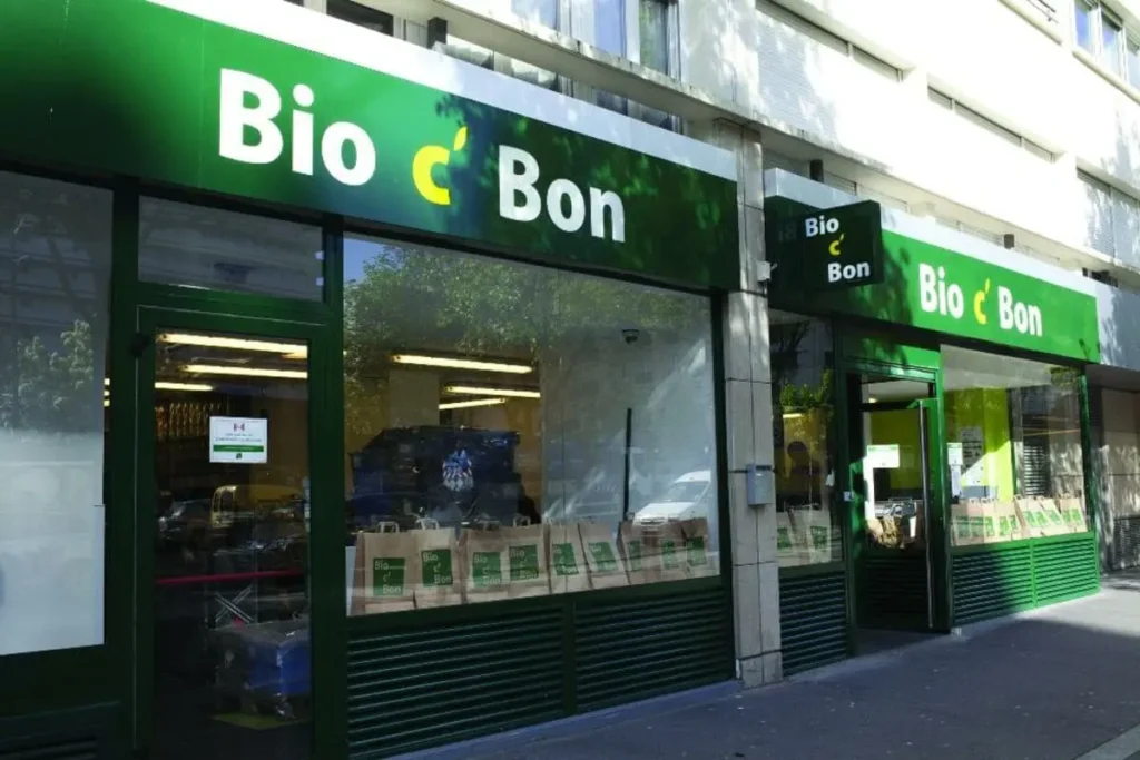 Devanture extérieure d'un magasin Bio c' Bon avec ses enseignes vertes distinctives et de grands sacs en papier visibles en vitrine.