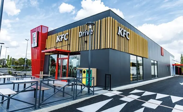 Façade moderne d'un restaurant KFC avec service au volant (Drive) et terrasse extérieure.