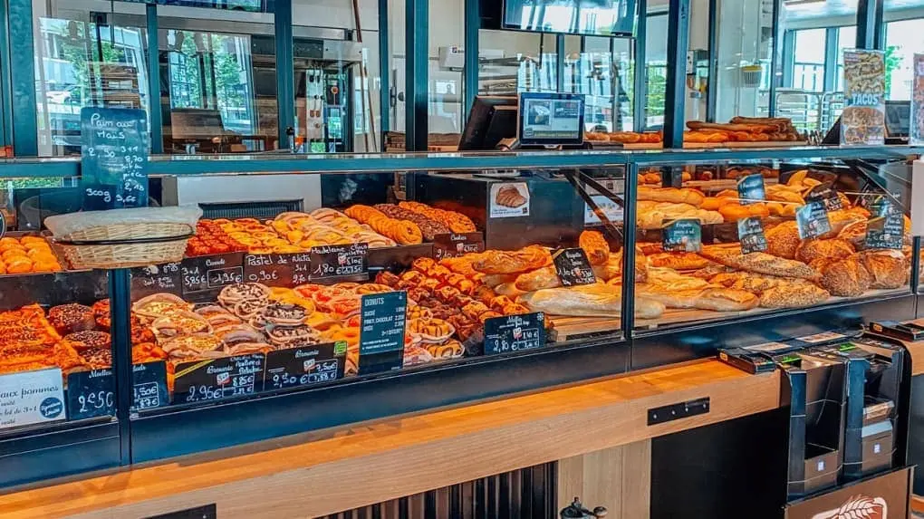 Vitrine réfrigérée de la Boulangerie Louise présentant une large sélection de viennoiseries (croissants, pains au chocolat, donuts) et de pains artisanaux avec étiquettes de prix.