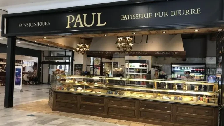 Façade noire traditionnelle de la boulangerie Paul dans une rue pavée, avec un auvent blanc et des colombages à l'étage.