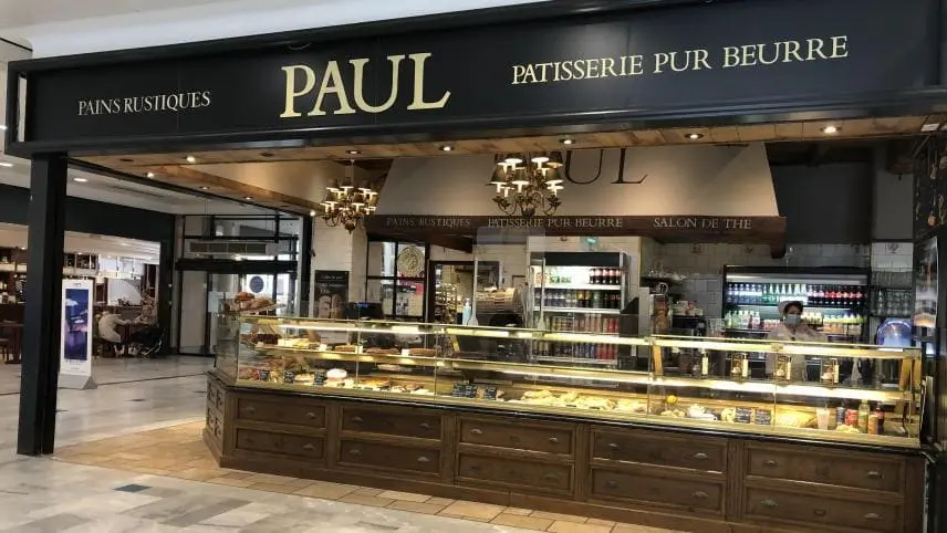 Façade noire traditionnelle de la boulangerie Paul dans une rue pavée, avec un auvent blanc et des colombages à l'étage.
