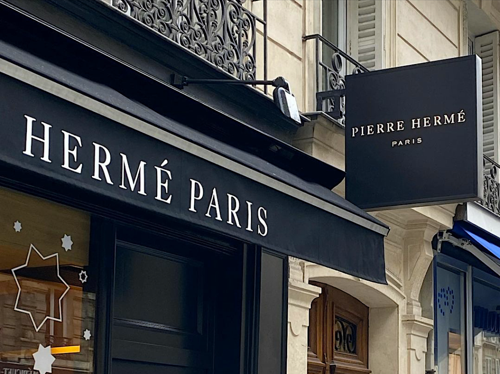 Enseigne noire et store extérieur de la pâtisserie Pierre Hermé Paris sur une façade de style haussmannien.