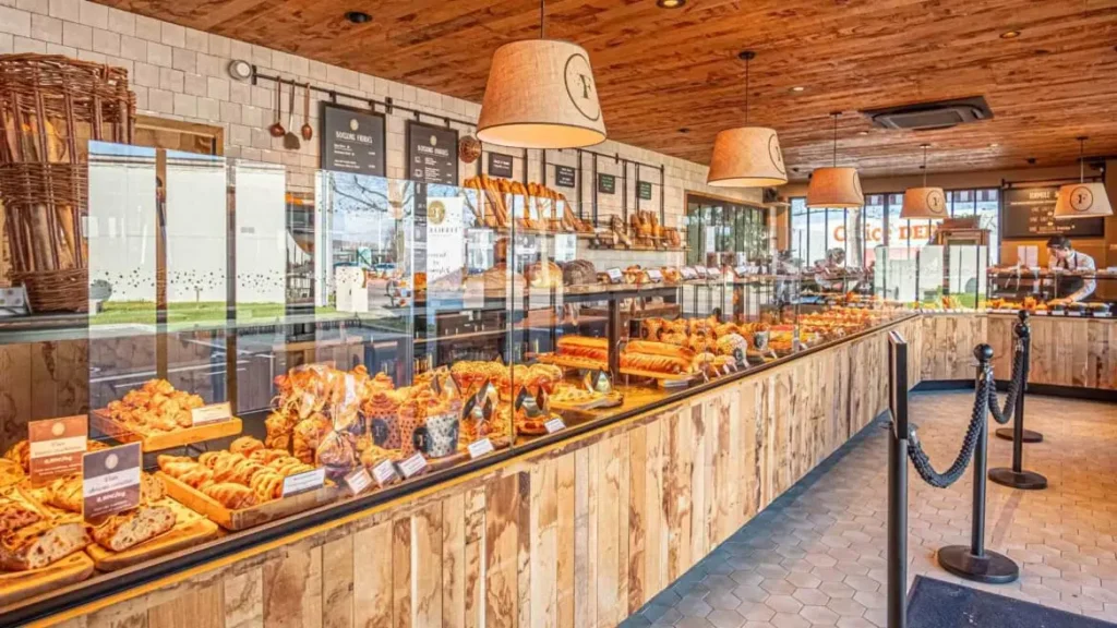 Intérieur d'une boulangerie Feuillette avec un large étalage de pâtisseries, viennoiseries et pains sous vitrine dans un décor boisé et chaleureux.