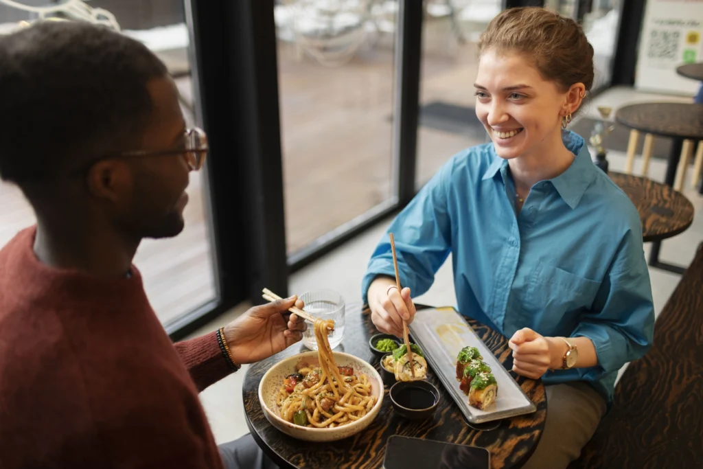 Un couple partageant des sushis et des nouilles dans un cadre convivial, une situation idéale pour apprendre comment manger sans gluten au restaurant en privilégiant la cuisine asiatique adaptée.