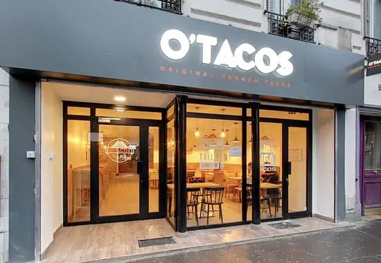 Devanture moderne d'un restaurant O'Tacos avec enseigne lumineuse et larges baies vitrées donnant sur l'intérieur éclairé.