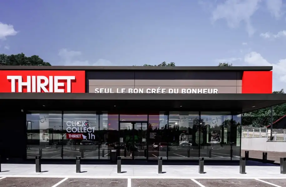 Façade moderne d'un magasin Thiriet avec l'enseigne rouge, le slogan 'Seul le bon crée du bonheur' et une affiche publicitaire pour le service Click and Collect en 1h.