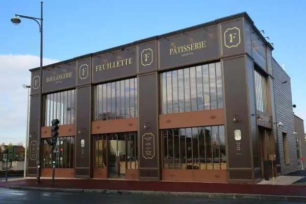 Façade extérieure d'une boulangerie pâtisserie Feuillette avec de grandes baies vitrées et une devanture élégante de couleur marron et dorée.