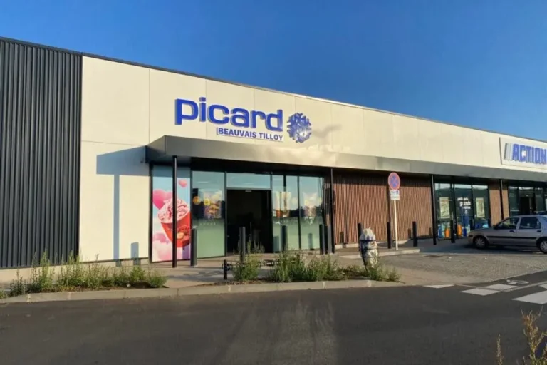 Façade extérieure d'un magasin Picard Surgelés situé à Beauvais Tilloy, avec son logo bleu caractéristique sur un bâtiment moderne blanc et gris, à côté d'une enseigne Action.