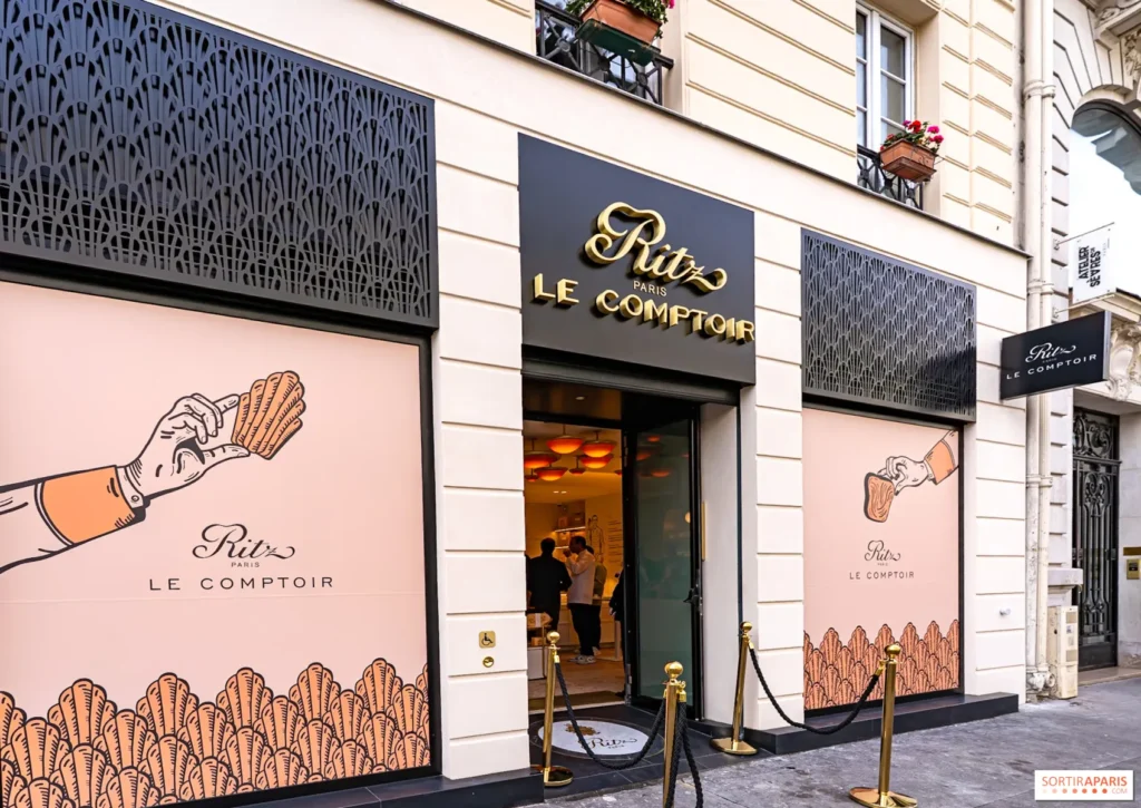 Façade de la boutique Ritz Paris Le Comptoir avec enseigne dorée, poteaux de guidage et vitrines décorées d'illustrations de madeleines.
