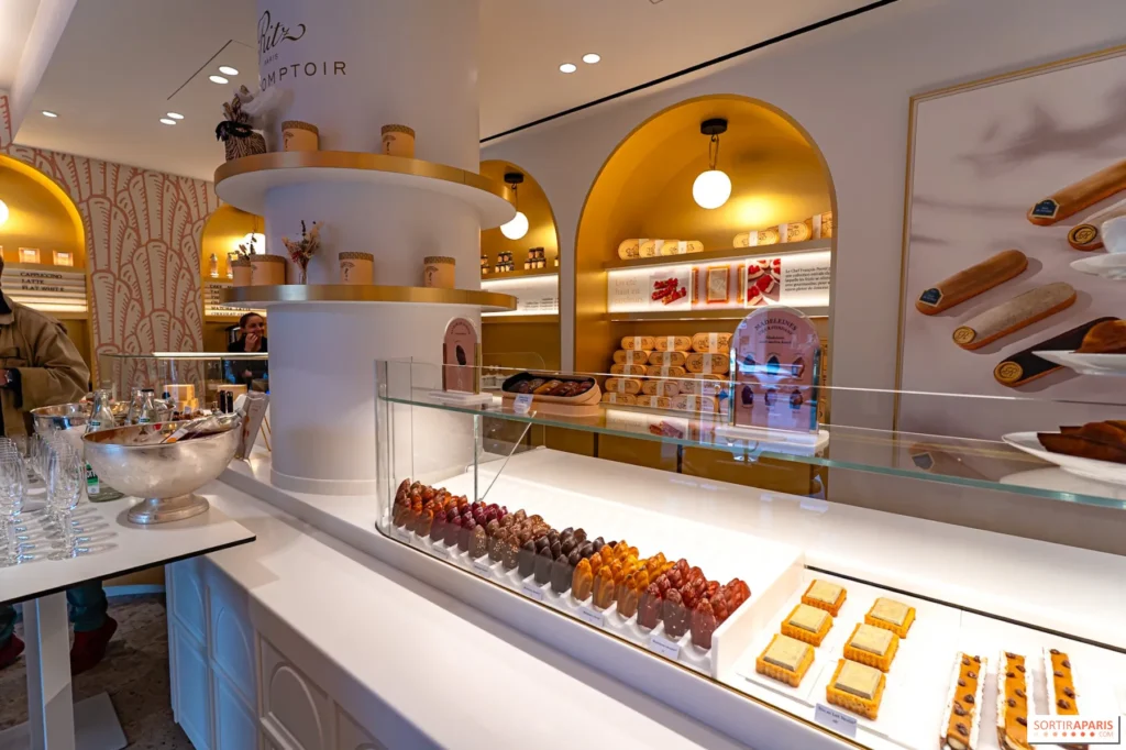Intérieur de la pâtisserie Ritz Paris Le Comptoir montrant un alignement de madeleines glacées et de pâtisseries fines sous une vitrine en verre.