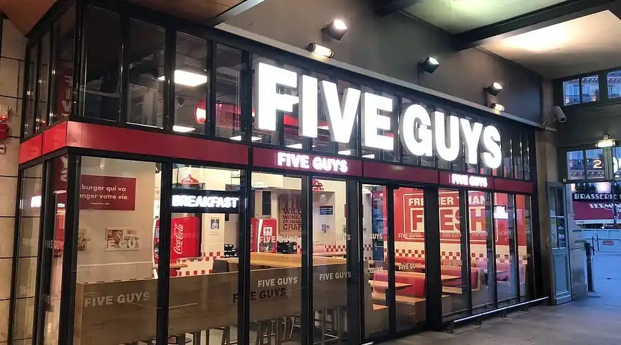 Devanture et enseigne lumineuse du restaurant de burgers Five Guys vue de l'extérieur