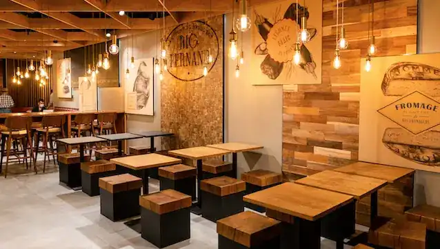 Intérieur chaleureux et décor rustique en bois du restaurant de burgers Big Fernand avec tables et tabourets hauts