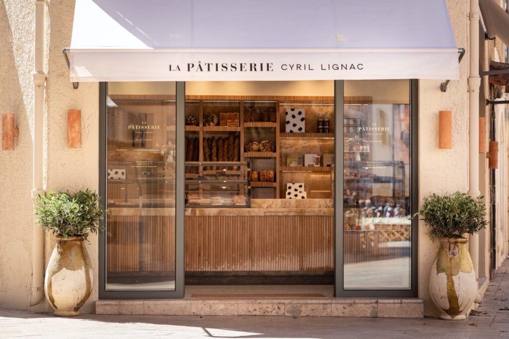 Entrée de La Pâtisserie Cyril Lignac à Saint-Tropez montrant des pains artisanaux, des baguettes et des boîtes cadeaux sur des étagères en bois et marbre.